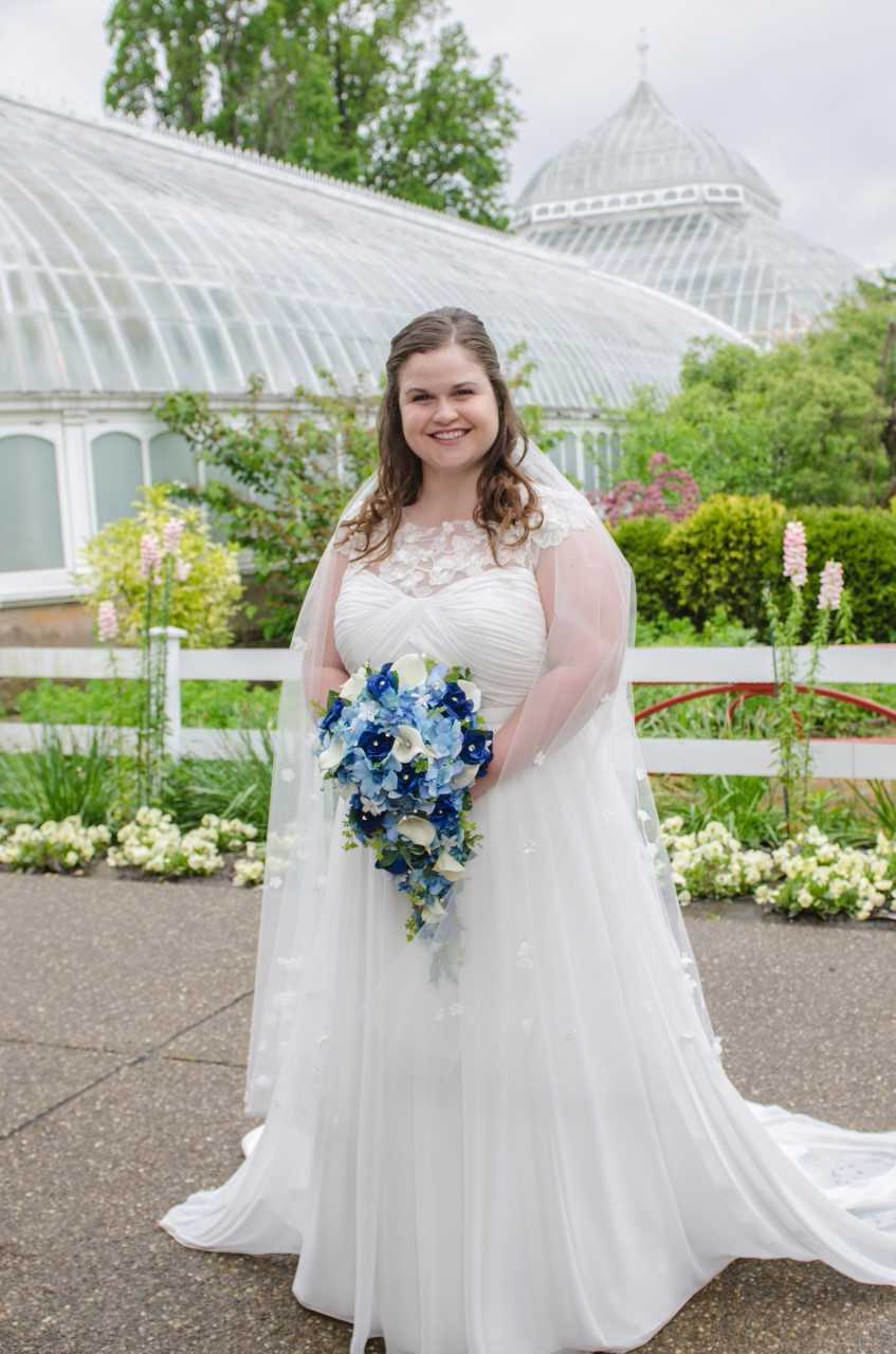 bride smiles with her blue cascade bouquet outside of phipps conservatory in pittsburgh