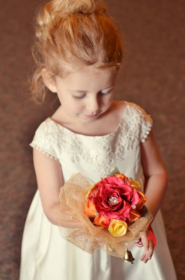 sweet flower girl admires her flower girl wand featuring a red rose